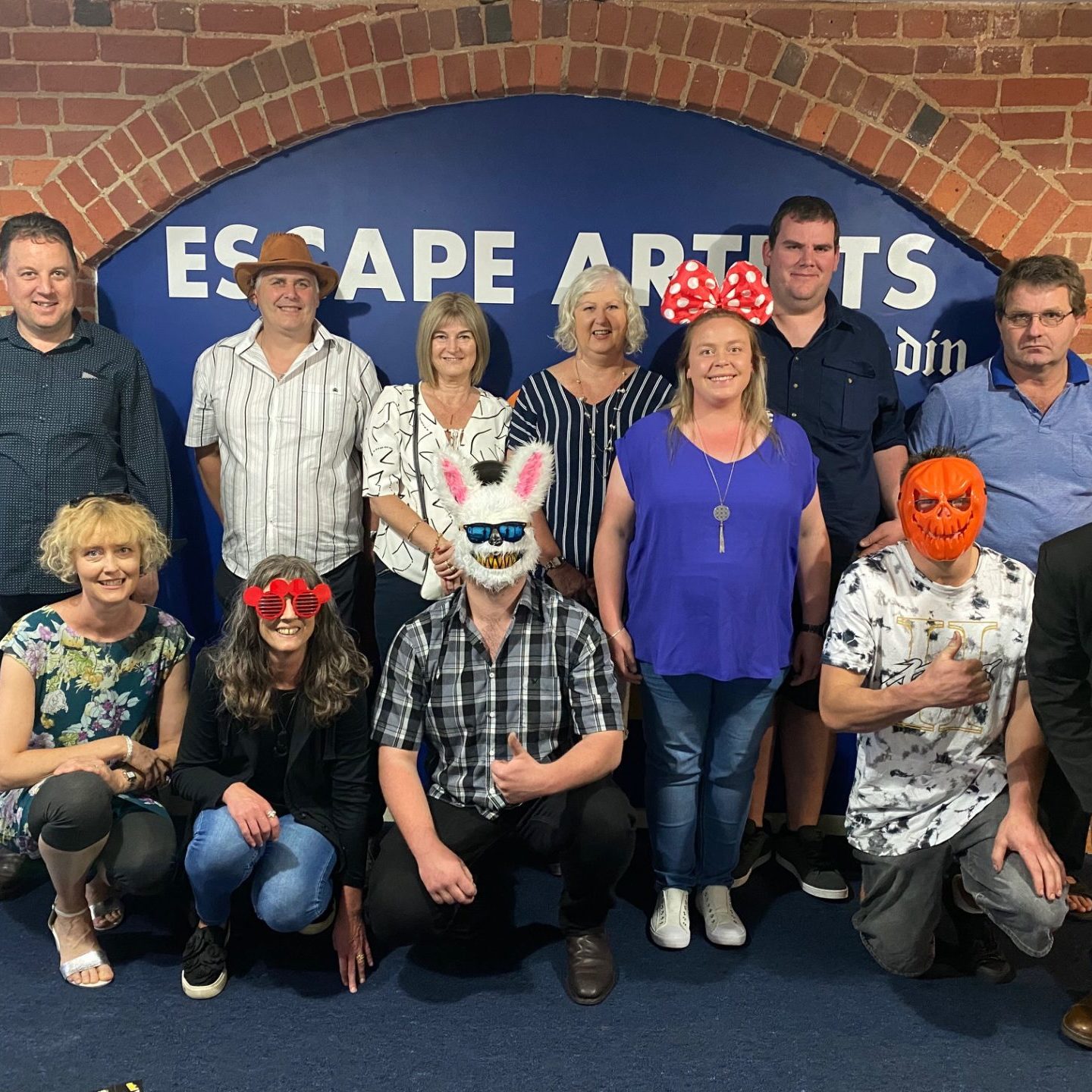 A workplace group at Escape Artists Dunedin in front of the brand wall after their games